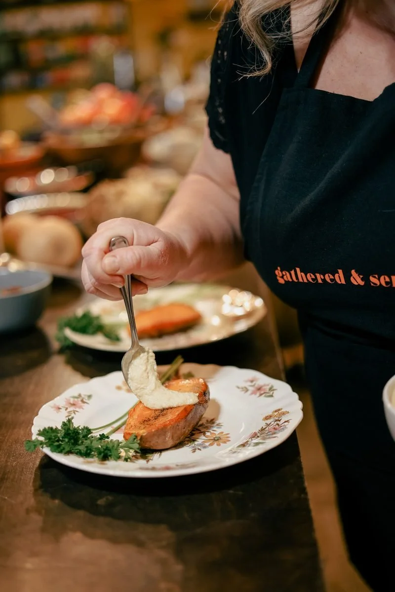 Chef adding a creamy sauce with a spoon onto a roasted sweet potato on a decorative plate