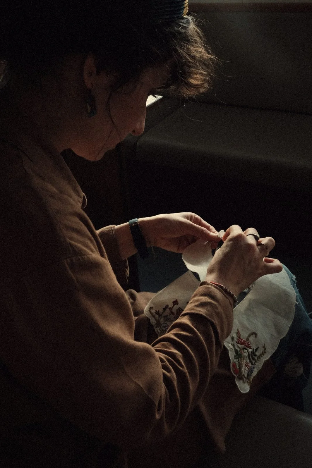 Woman hand stitching intricate embroidery on white fabric by window natural light