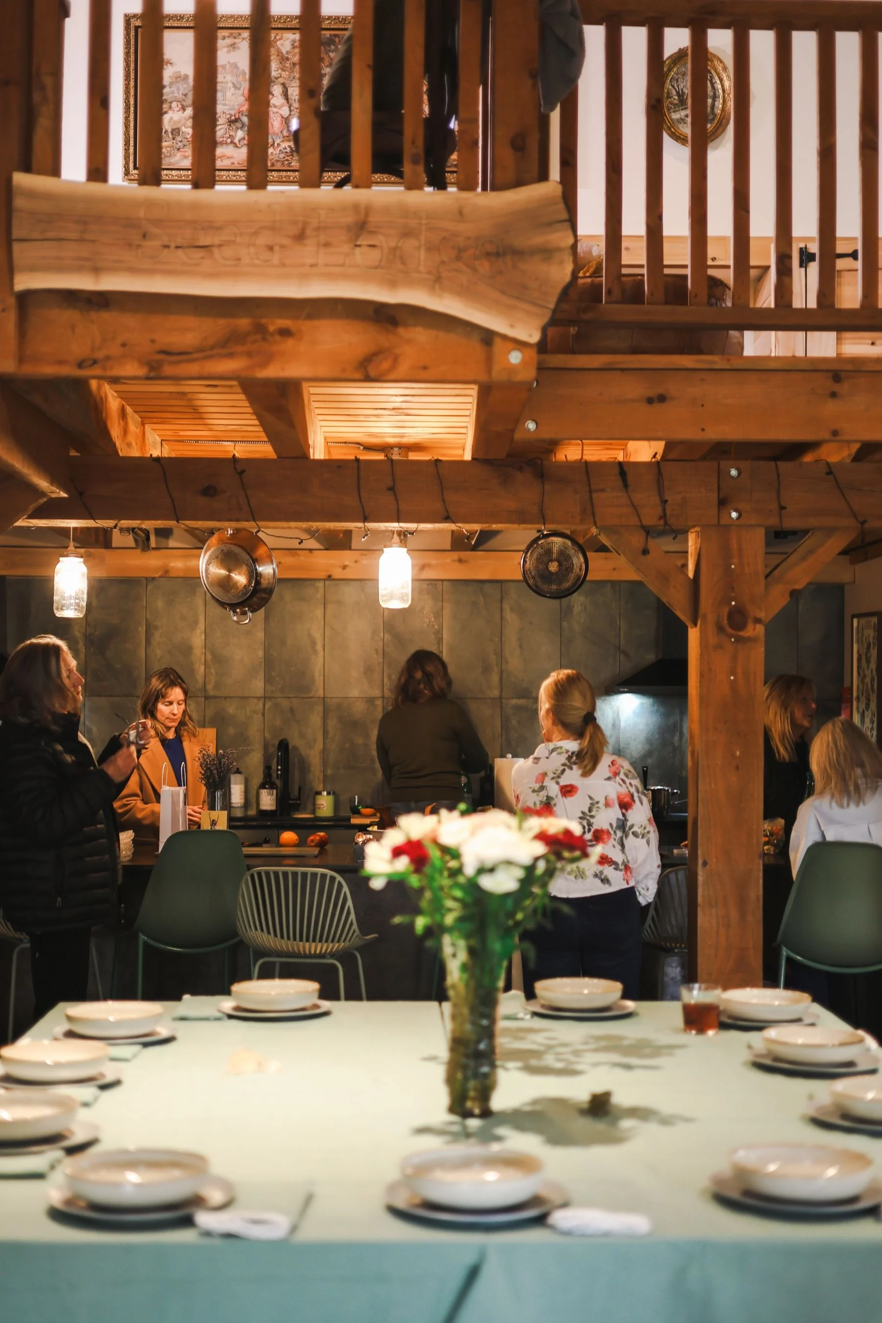 People gathering in a rustic wooden lodge kitchen with a set dining table in the foreground