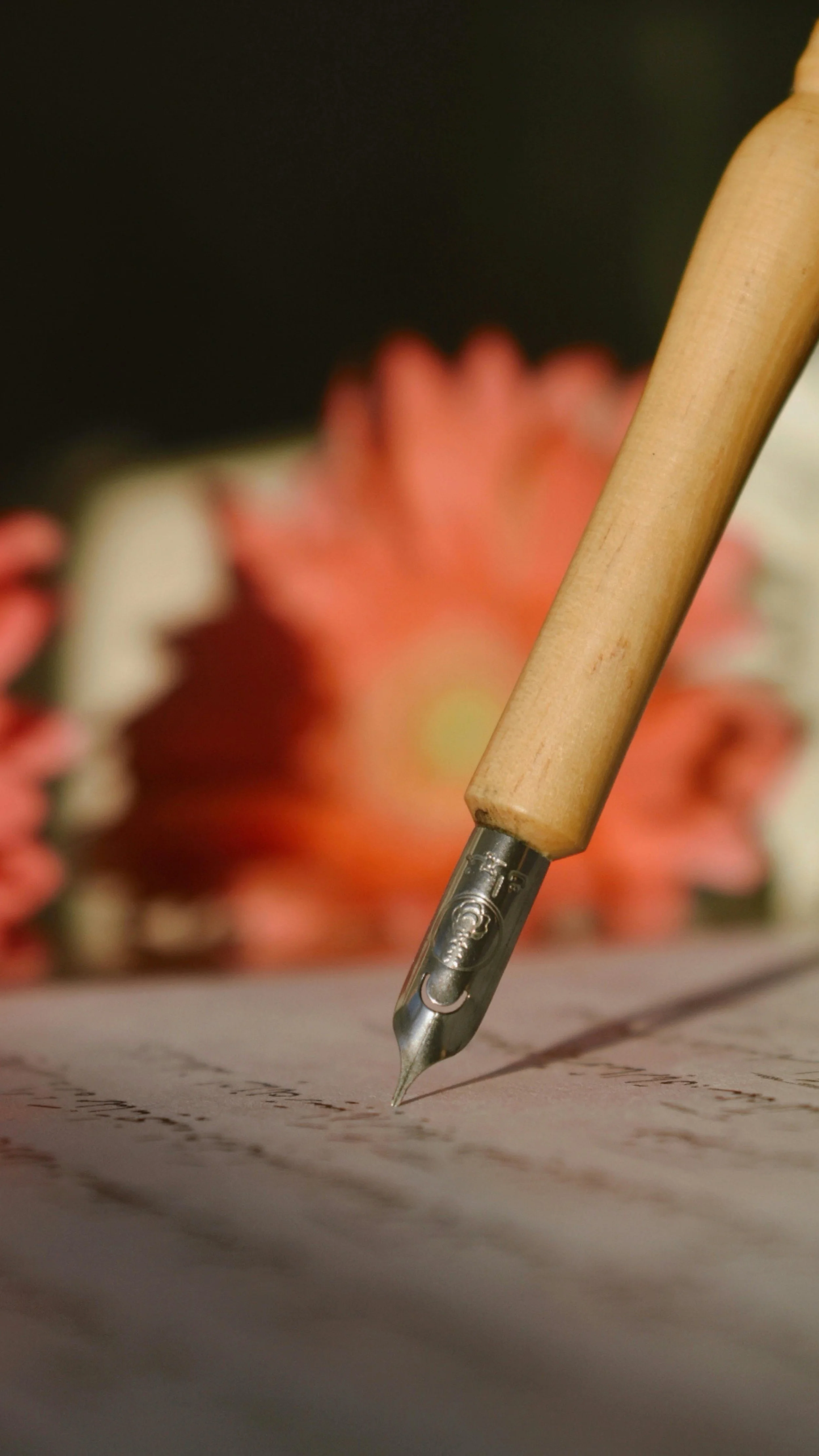 Close-up of a fountain pen writing on paper, with a blurred background of pink flowers.