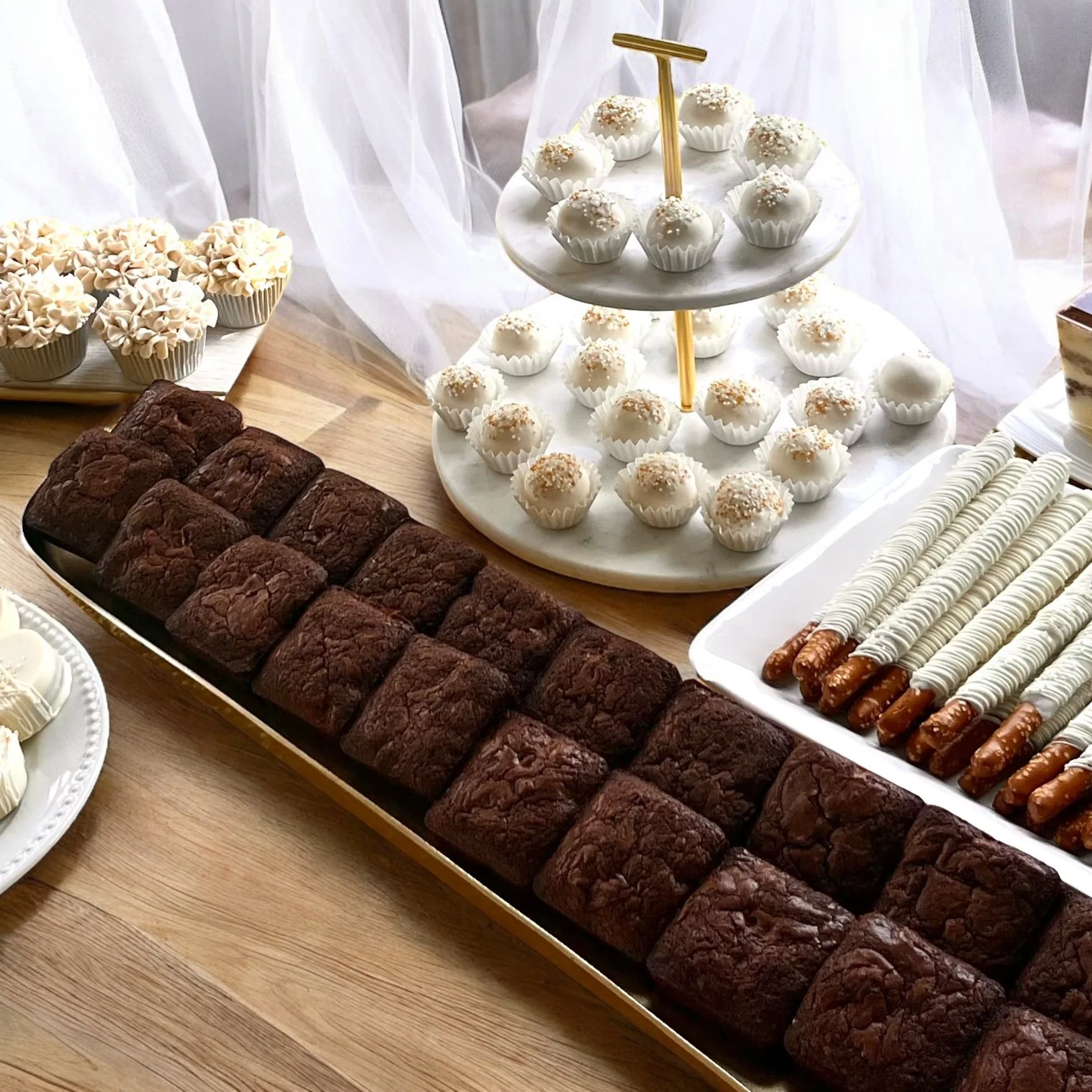 A display of wedding desserts, brownies, cake truffles, chocolate covered pretzel sticks and cupcakes