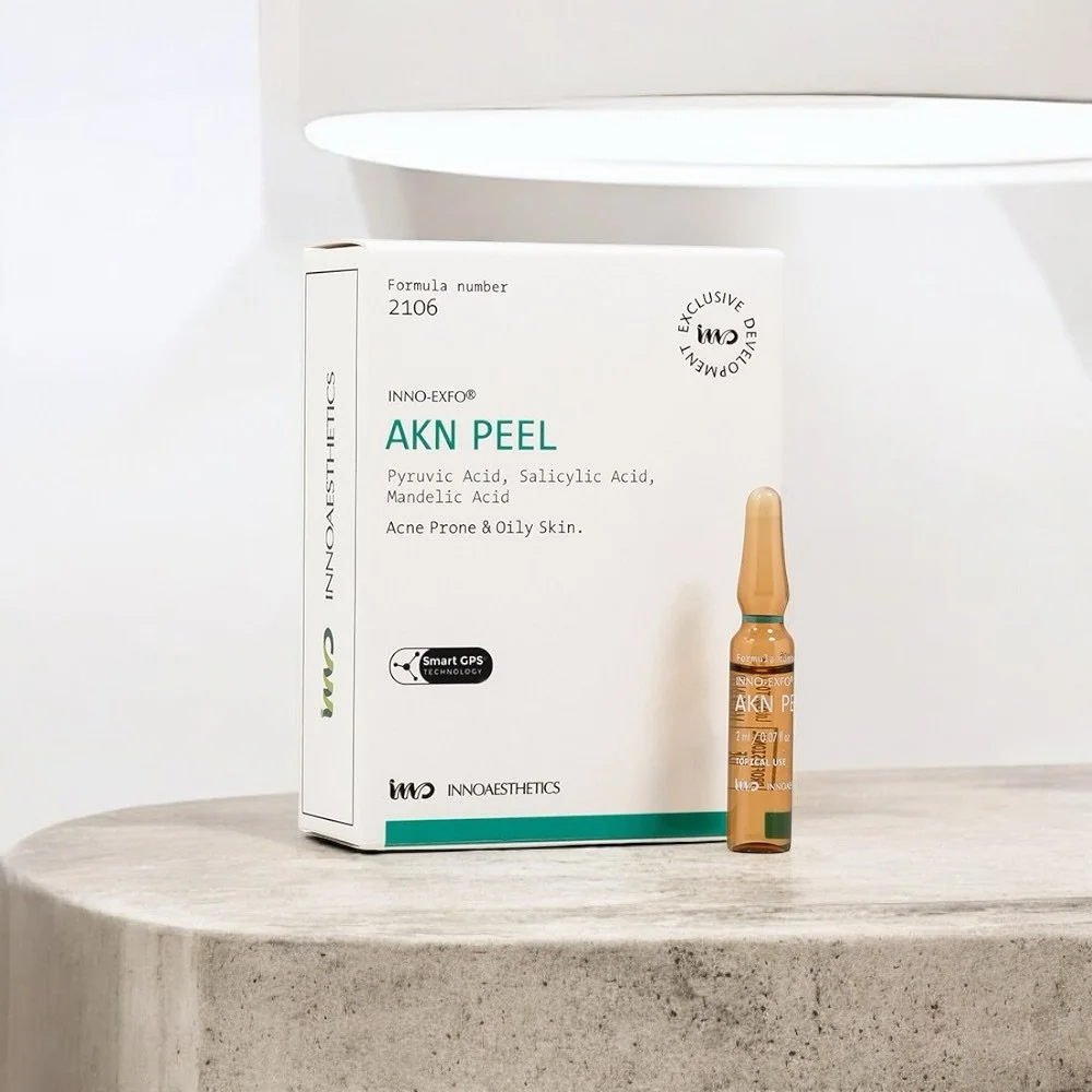 A box of INNO-AESTHETICS AKN Peel with a small ampoule in front of it, placed on a gray surface against a white background.
