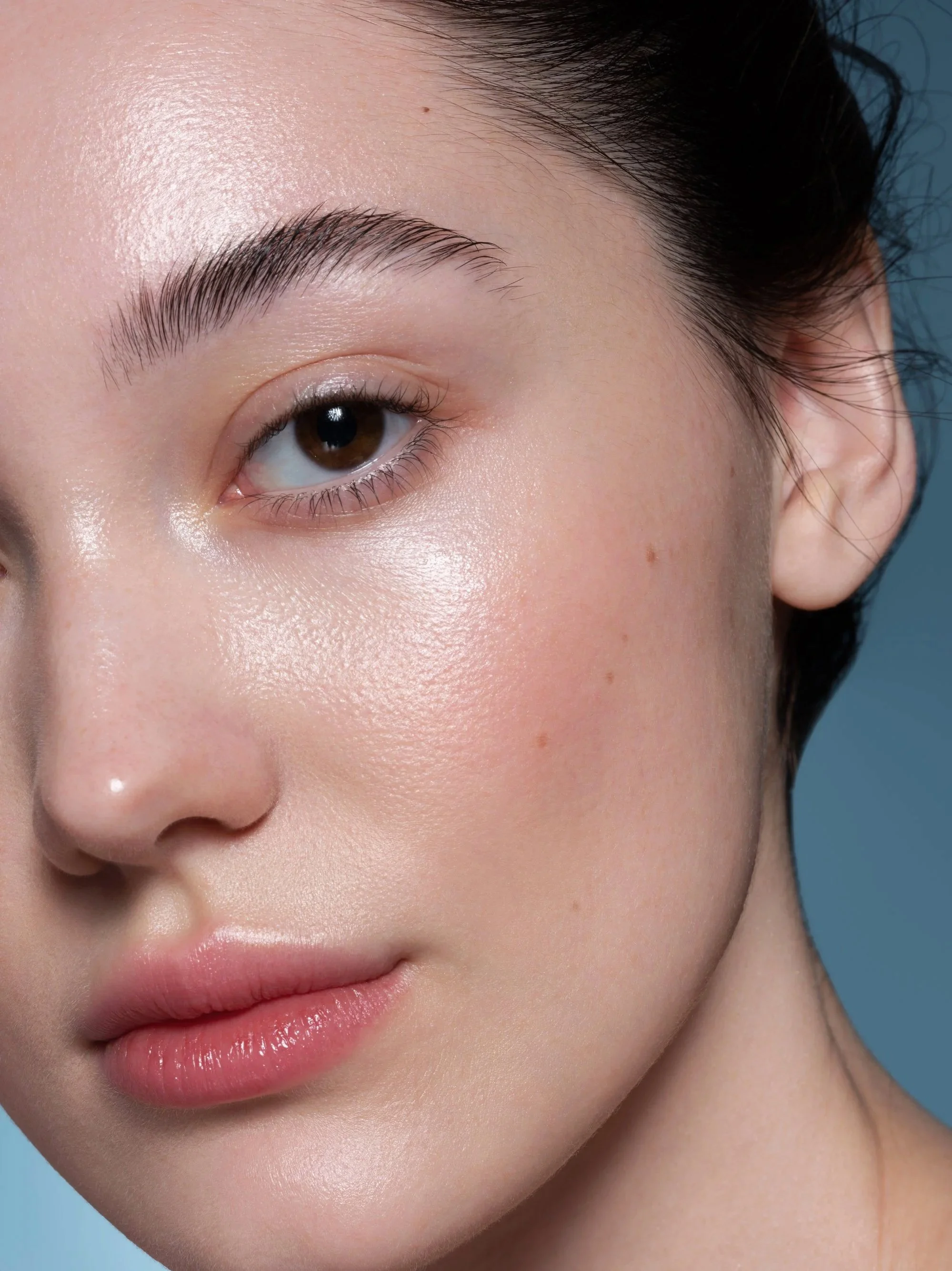 Close-up of a young woman's face showing her eye, eyebrow, cheek, and part of her lips with smooth skin and natural makeup.