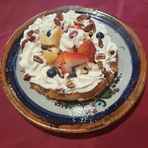 A waffle topped with whipped cream, fresh fruit and pecans