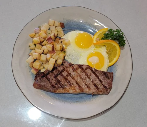 Grilled steak with two fried eggs and country potatoes