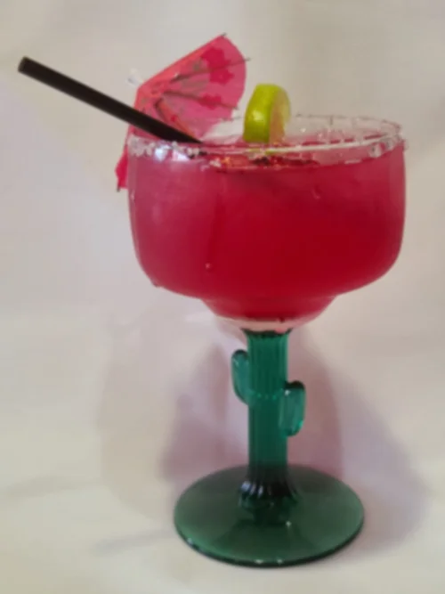 A pink margarita in a cactus-stem glass with a lime wedge and cocktail umbrella