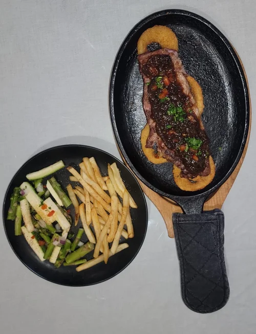 New York strip steak on a sizzling skillet, with fries and vegetables on the side