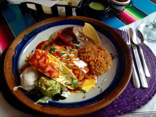 Combination plate with a crispy taco, an enchilada, Spanish rice, refried beans, guacamole and sour cream