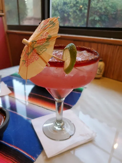 A pink margarita with a chile-salt rim, lime wheel and paper umbrella on a colorful sarape table runner