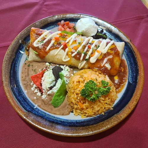 A burrito covered in ranchera sauce and crema, with Spanish rice and refried beans