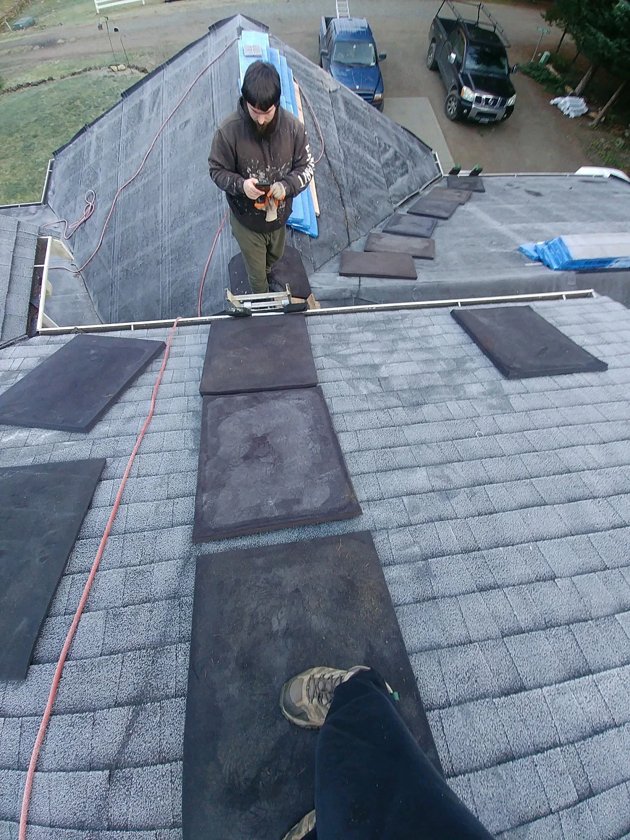 A worker standing on a roof inspecting solar panel installation, with his foot and part of his body visible in the foreground, while others are installing or working on the solar panels on the roof.