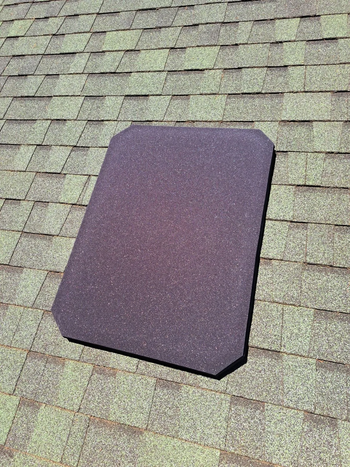 A black rectangular object with rounded corners placed on a shingled roof.