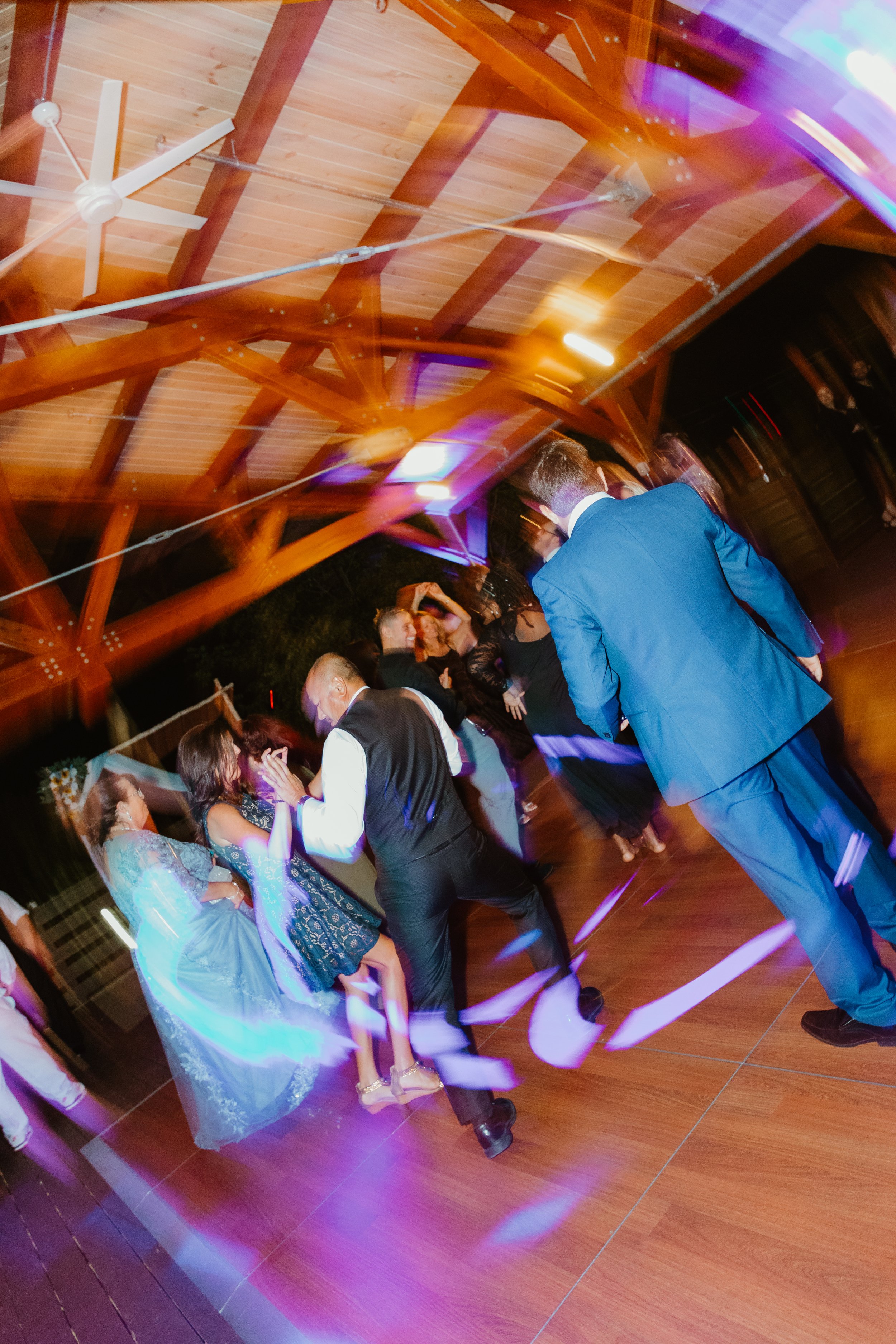 People dancing at a celebration or party in a decorated venue with a wooden ceiling.