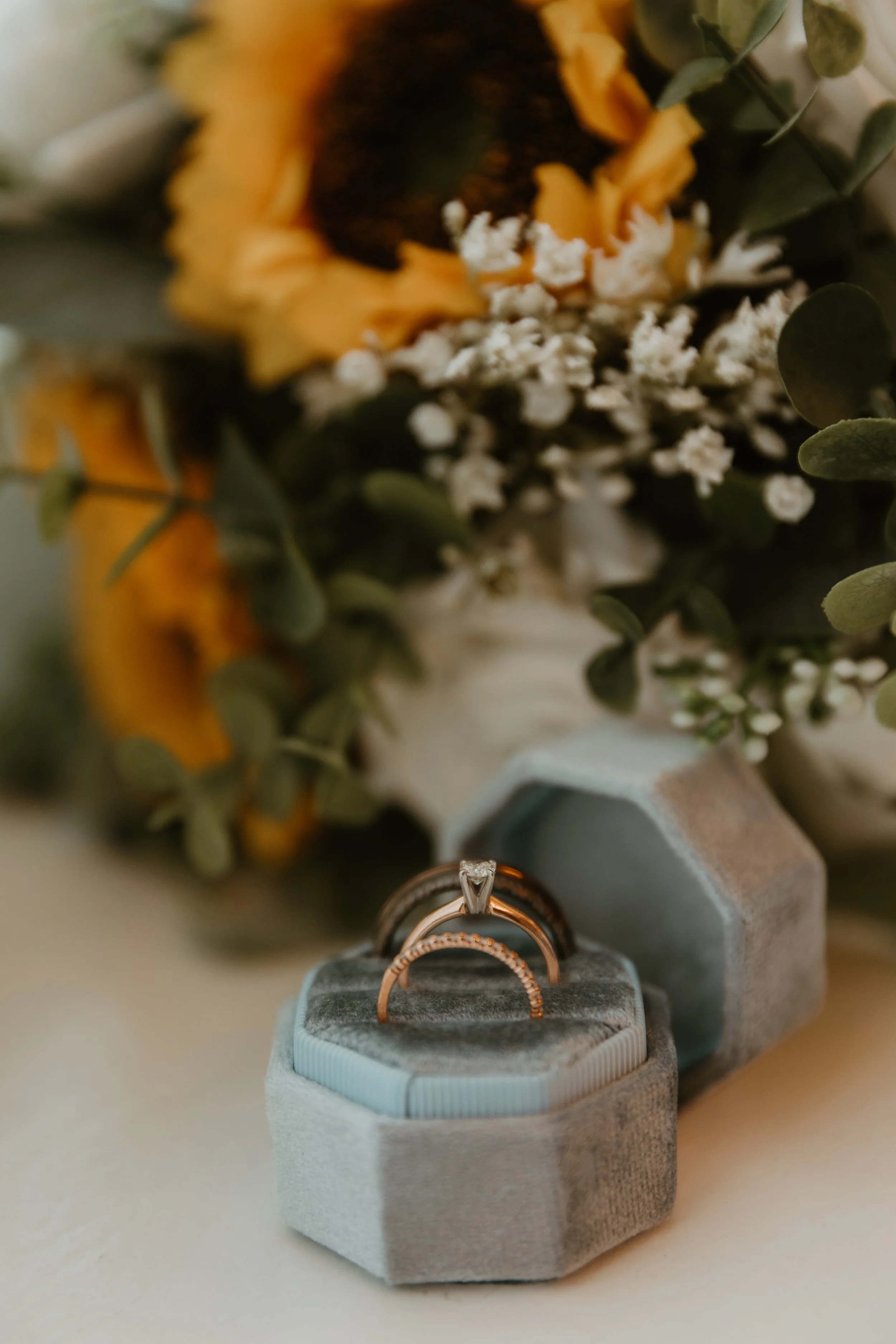 Three rings in an open jewelry box with a bouquet of flowers in the background.