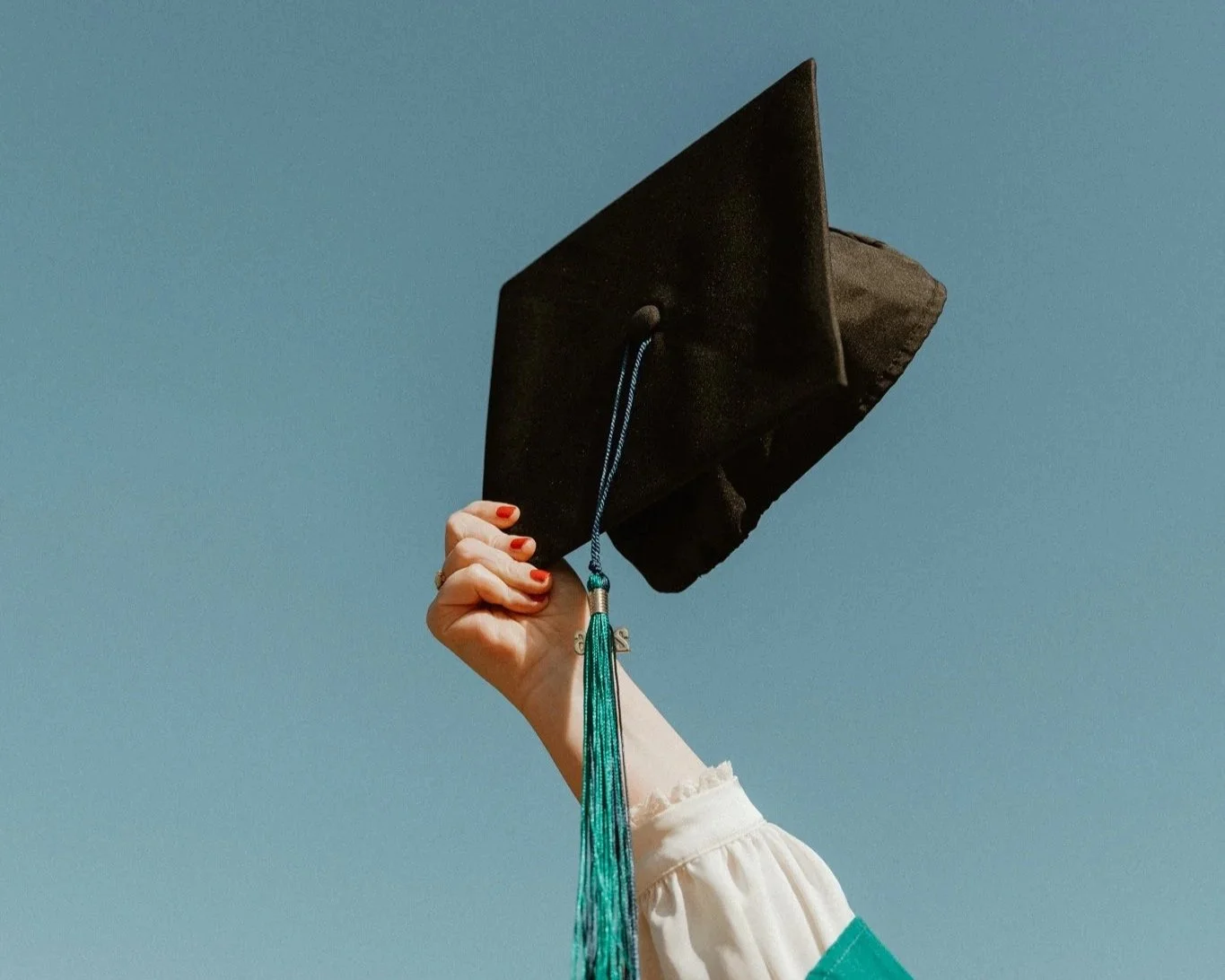 A young woman in graduation cap and gown standing in front of a fountain with columns during autumn.