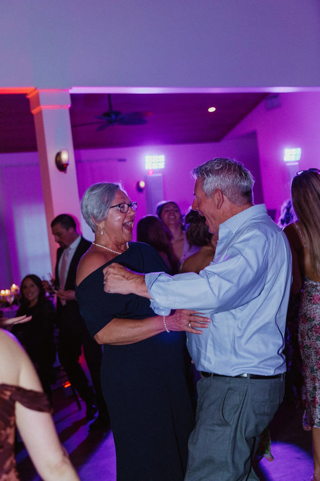 Older woman and man dancing closely at a social event with purple lighting.