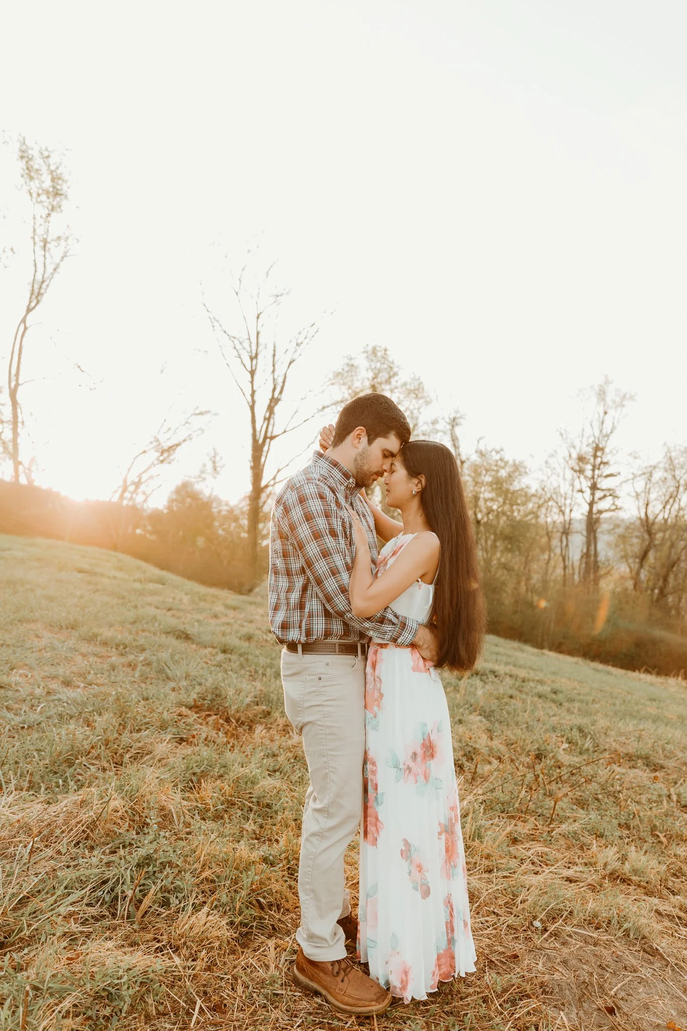 A man and woman standing outdoors in a forest, holding a newborn baby, with the man cradling the baby and the woman smiling at them.