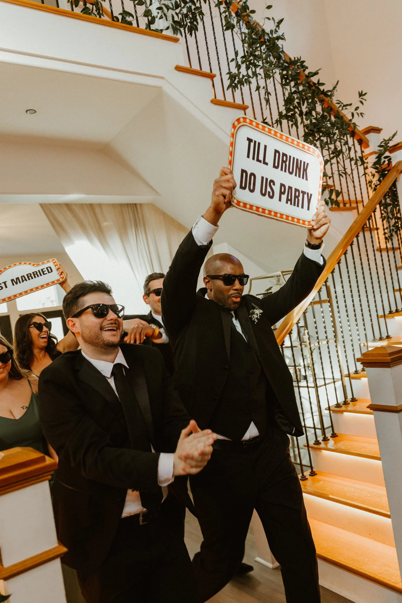 Group of people at a celebration, with one person holding a sign that says, 'TILL DRUNK DO US PARTY.'
