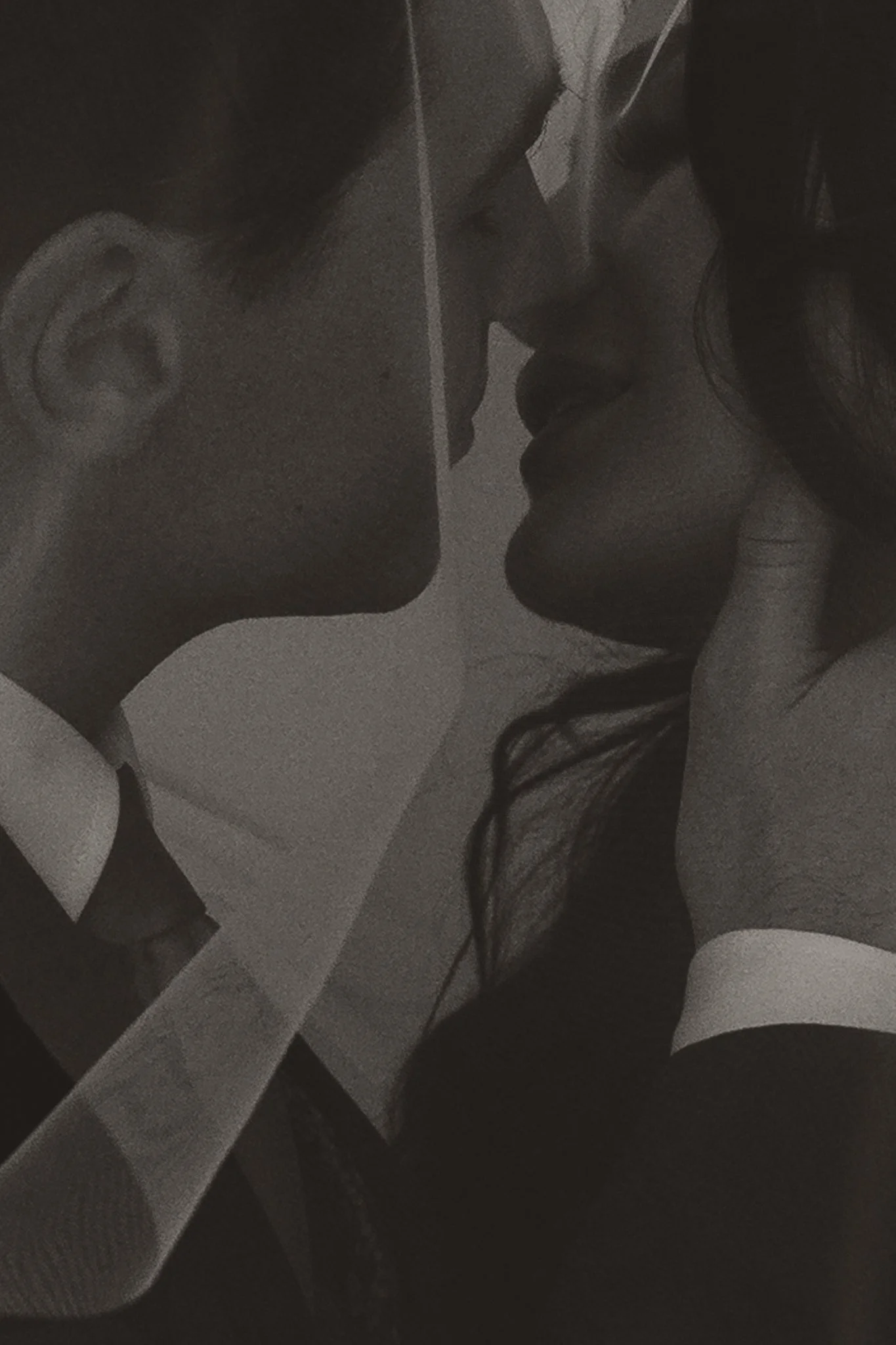 A black-and-white photo of a man and woman close to each other, about to kiss. The man is wearing glasses and a collared shirt, while the woman has dark hair, wears lipstick, and has her hand gently touching her face.