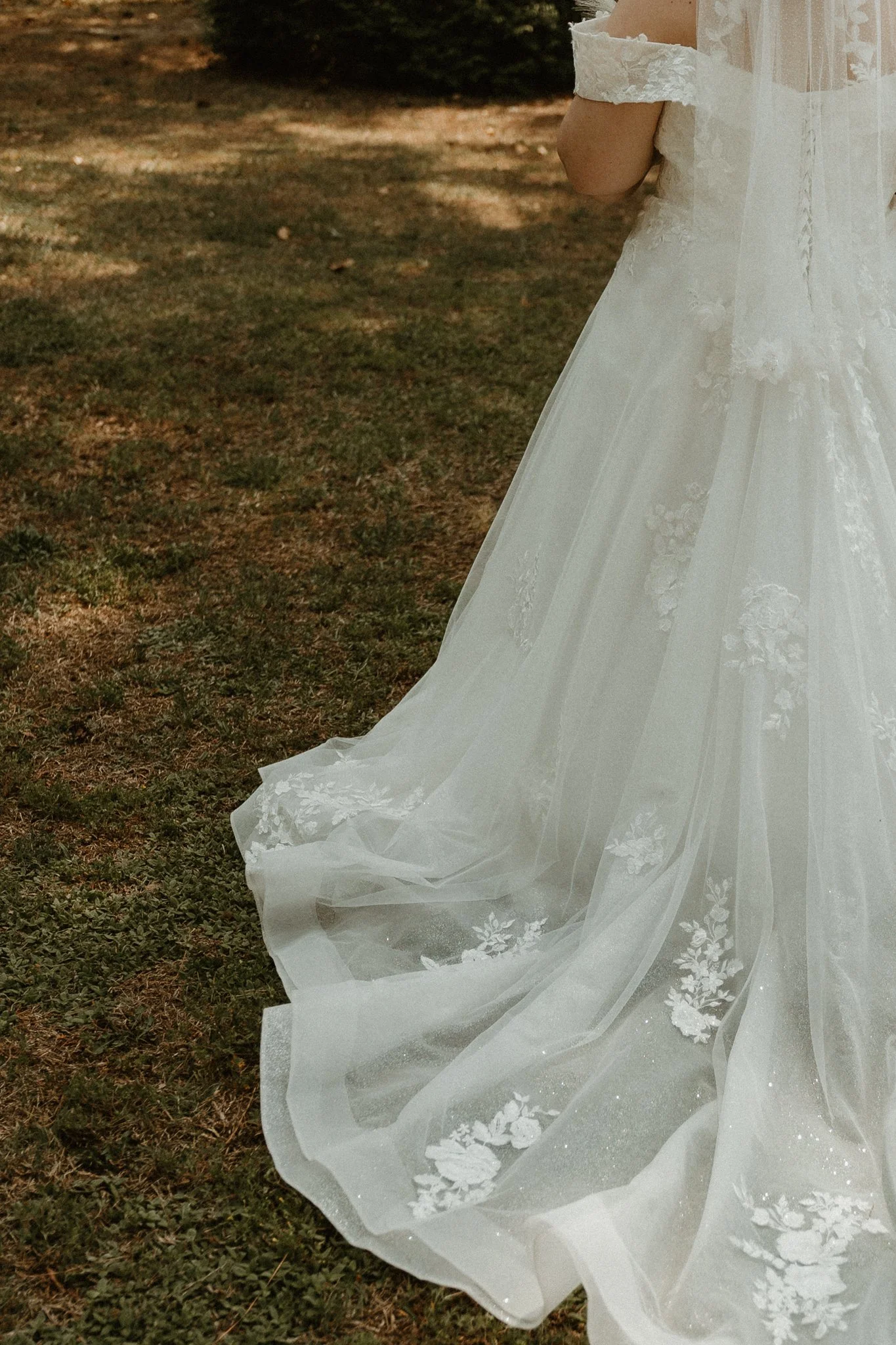 A white wedding dress with floral lace details, lying on the ground outdoors with grass and dirt.