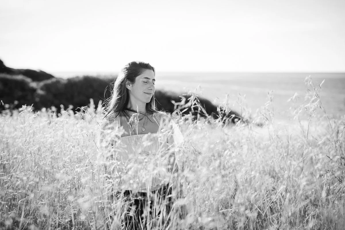 A woman standing in a grassy field with her eyes closed, enjoying the sunlight on a clear day.