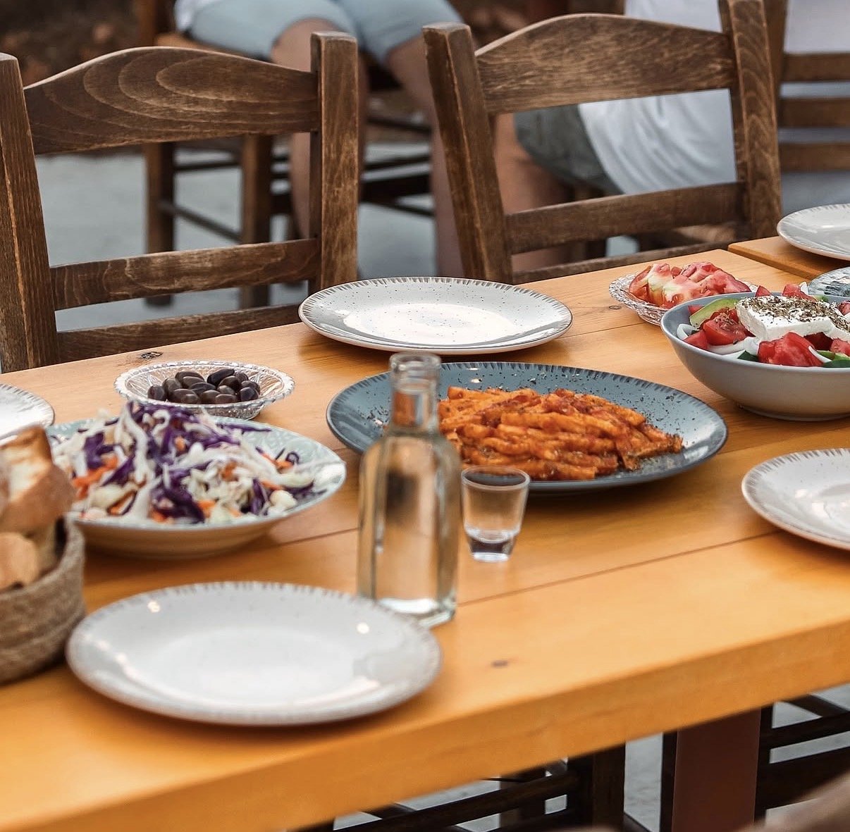 Mediterranean restaurant table with grilled vegetables, Greek salad, coleslaw, olives, sliced tomatoes, plates, and water glasses