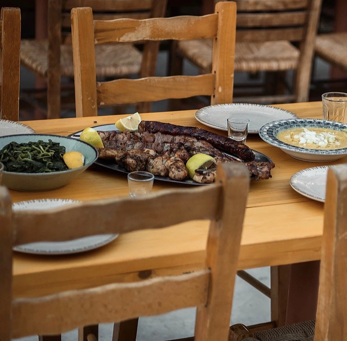 Grilled meat platter with sausage, lemon wedges, greens, and dipping sauce on a wooden restaurant table