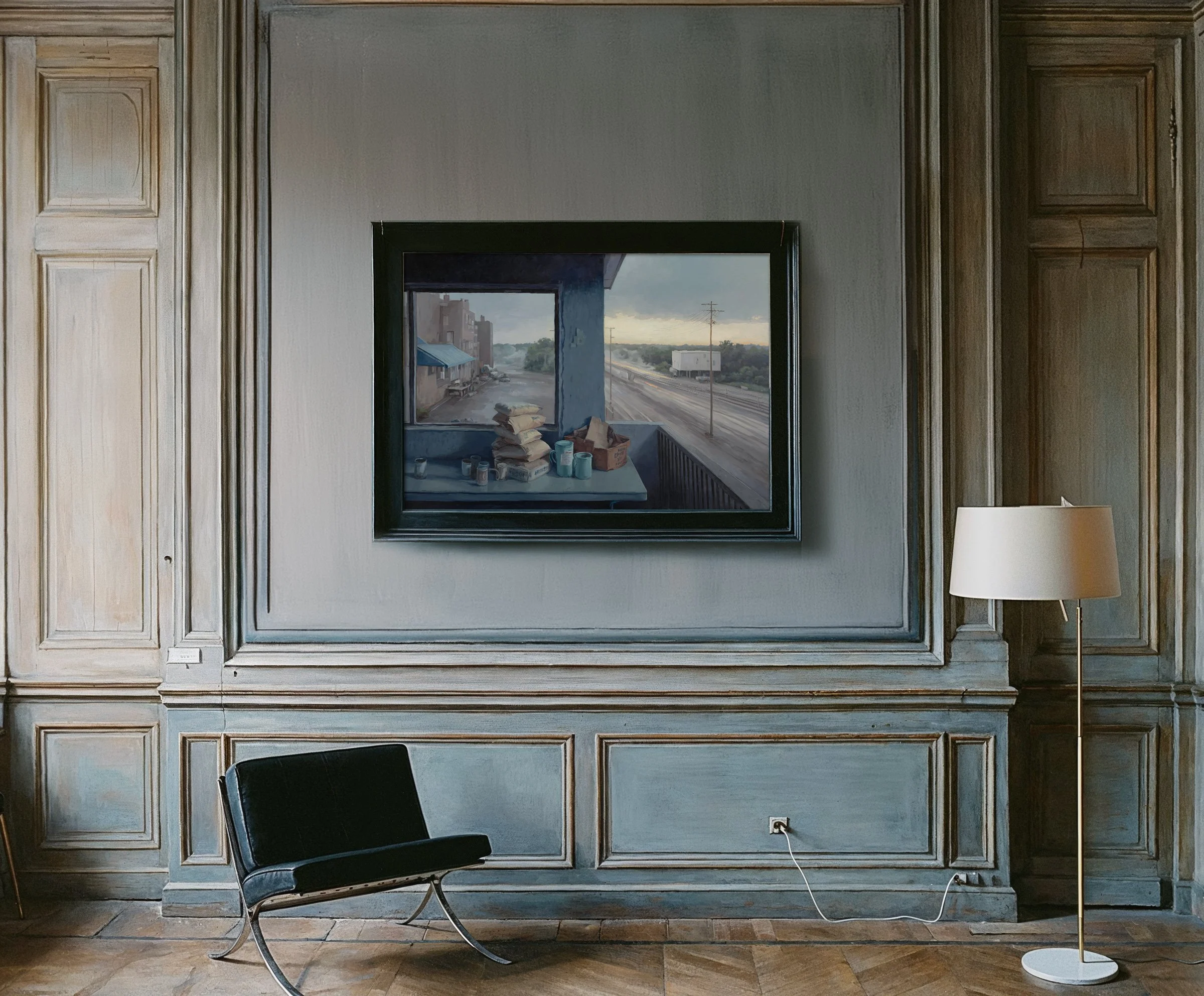 A room with wood-paneled walls and a hardwood floor, a black modern lounge chair, a white floor lamp, and a framed painting of a street scene with trucks and buildings on the wall.