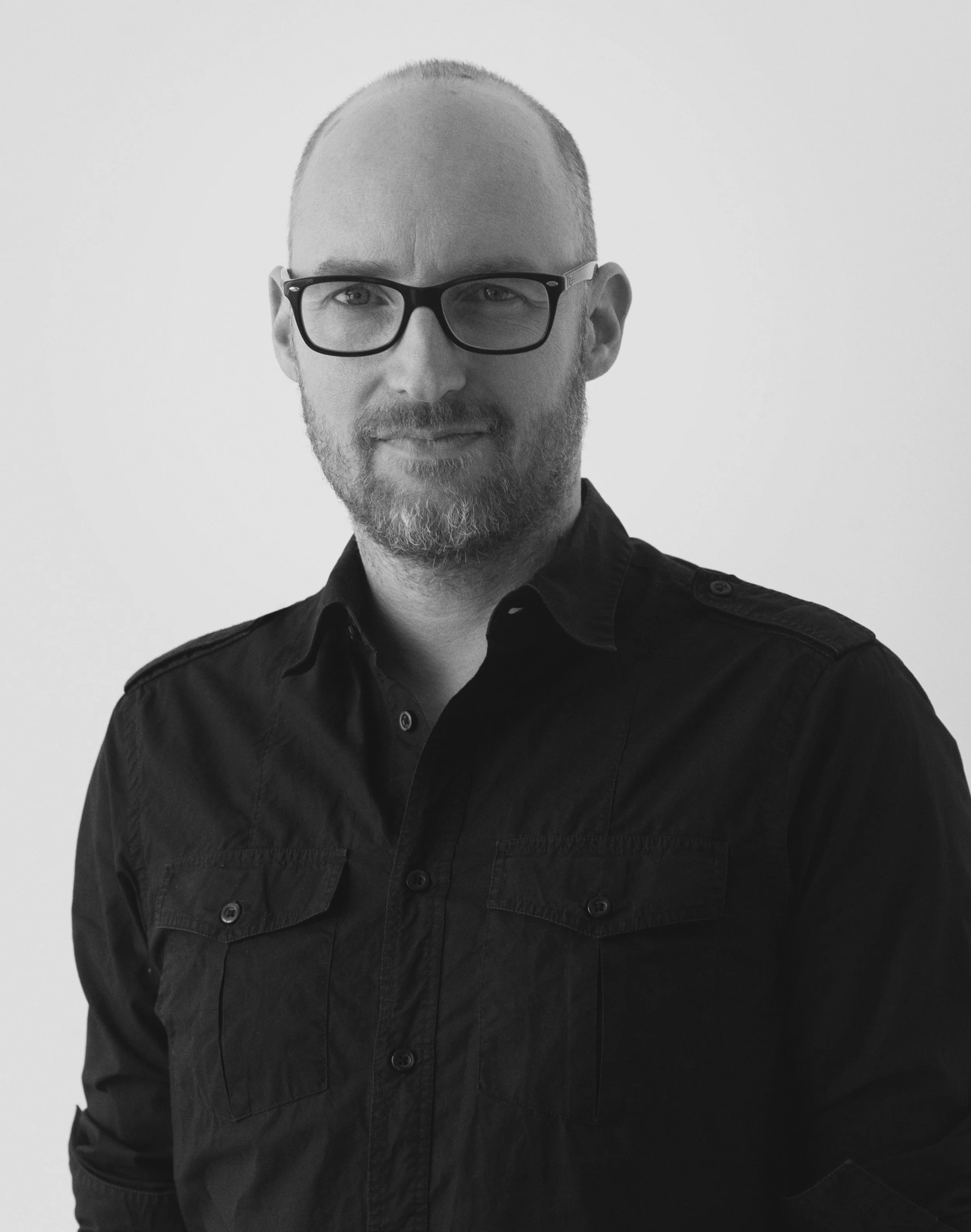A man with glasses and a beard, wearing a black button-up shirt, looking at the camera.