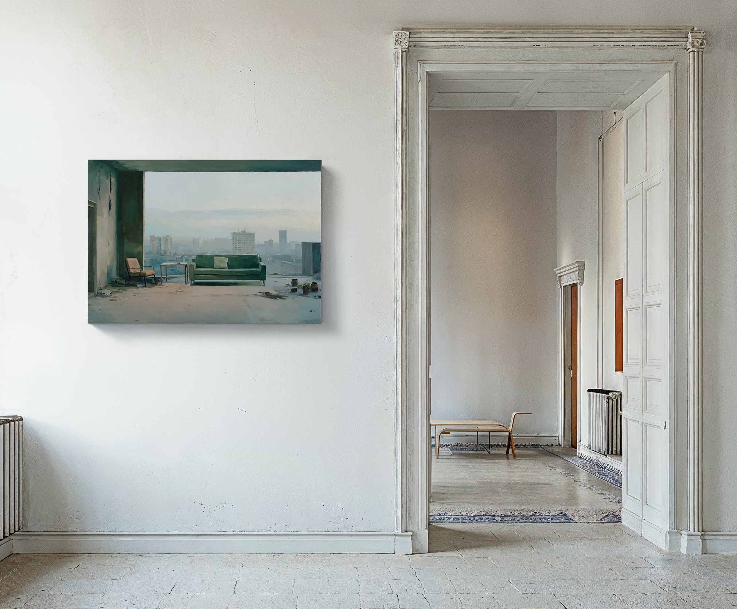 Interior of an old, minimally decorated apartment with white walls and tiled floor, featuring a framed painting of a city view with a green sofa and chairs in front of a large window, and doorway leading to a room with a low wooden bench and radiator