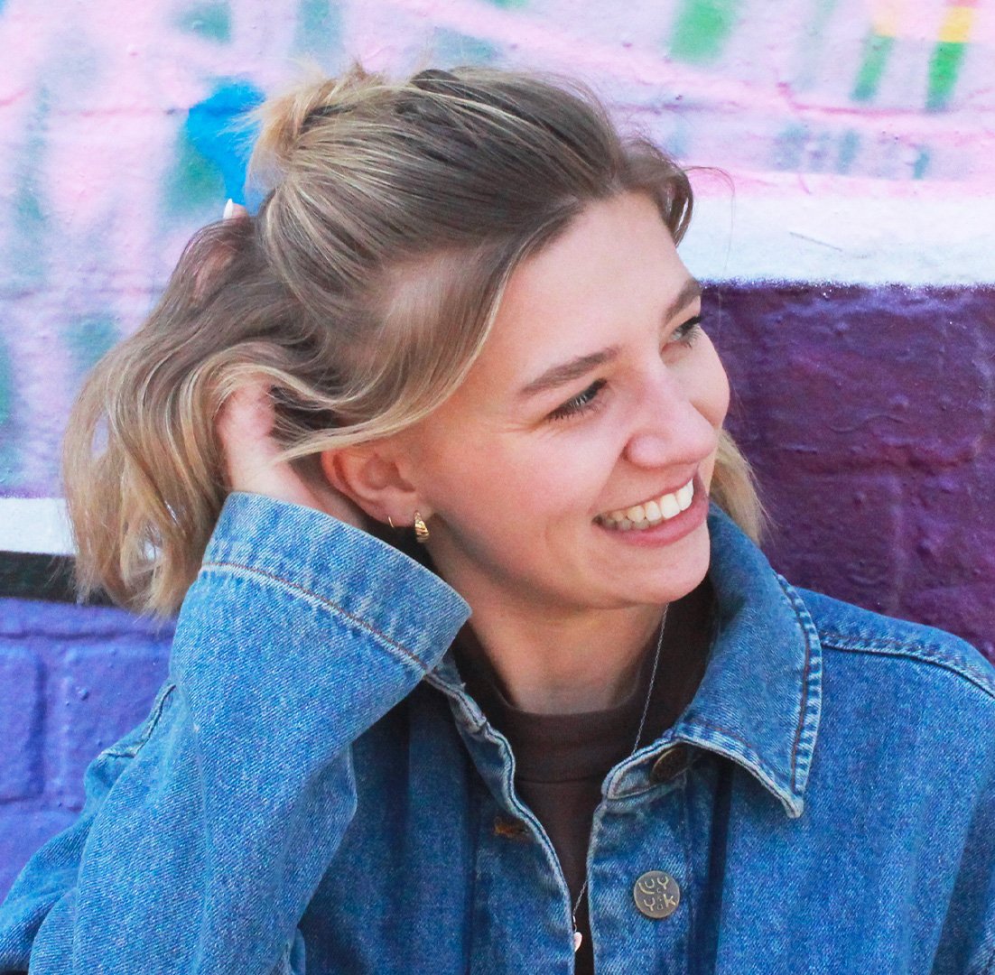 Lark’s designer, Oli, has bobbed blonde hair and is wearing a denim jacket in front of a graffiti-covered brick wall.