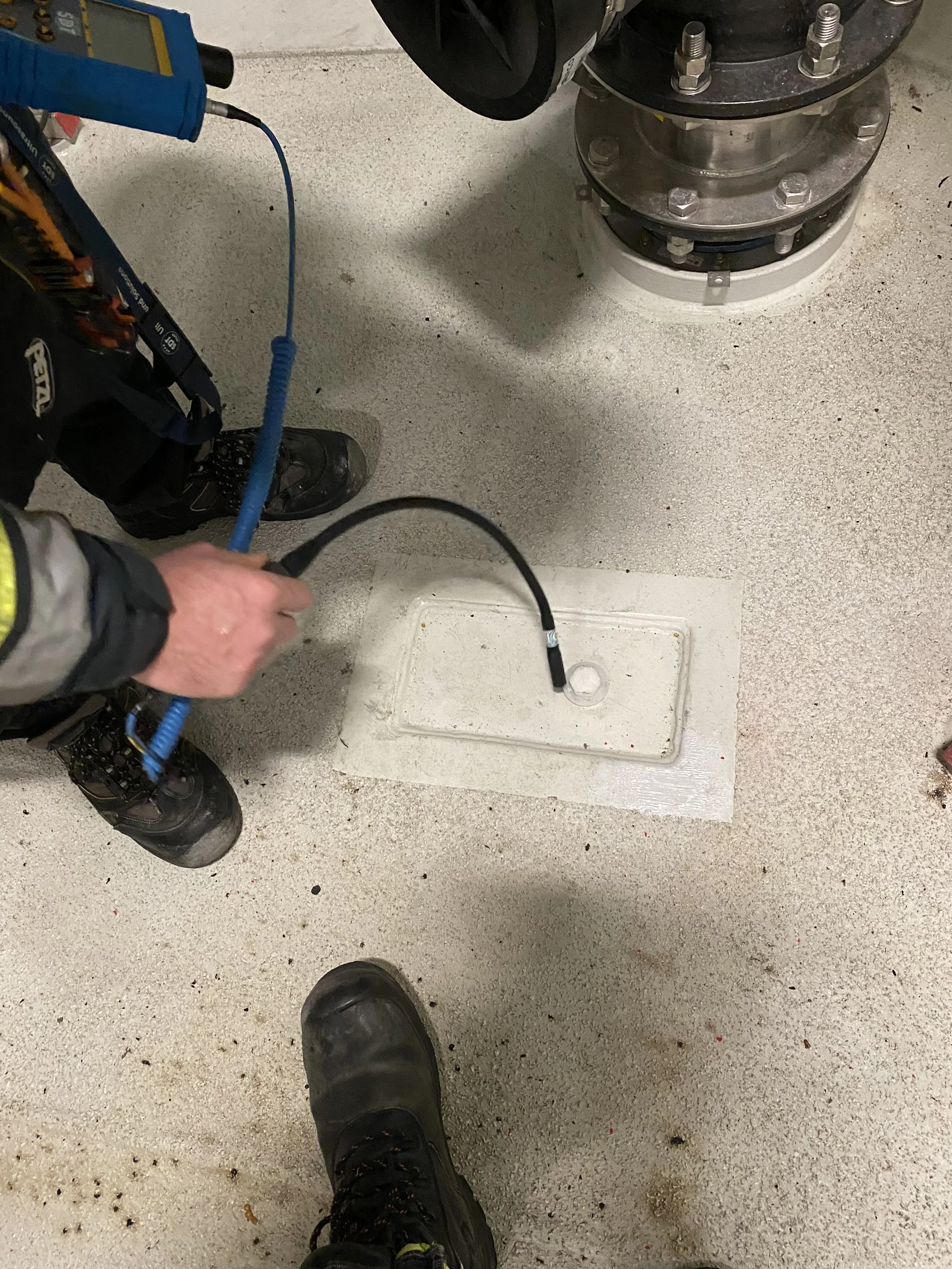 Person in safety gear testing a fuel tank or pipe with a gauge in an industrial or mechanical setting.