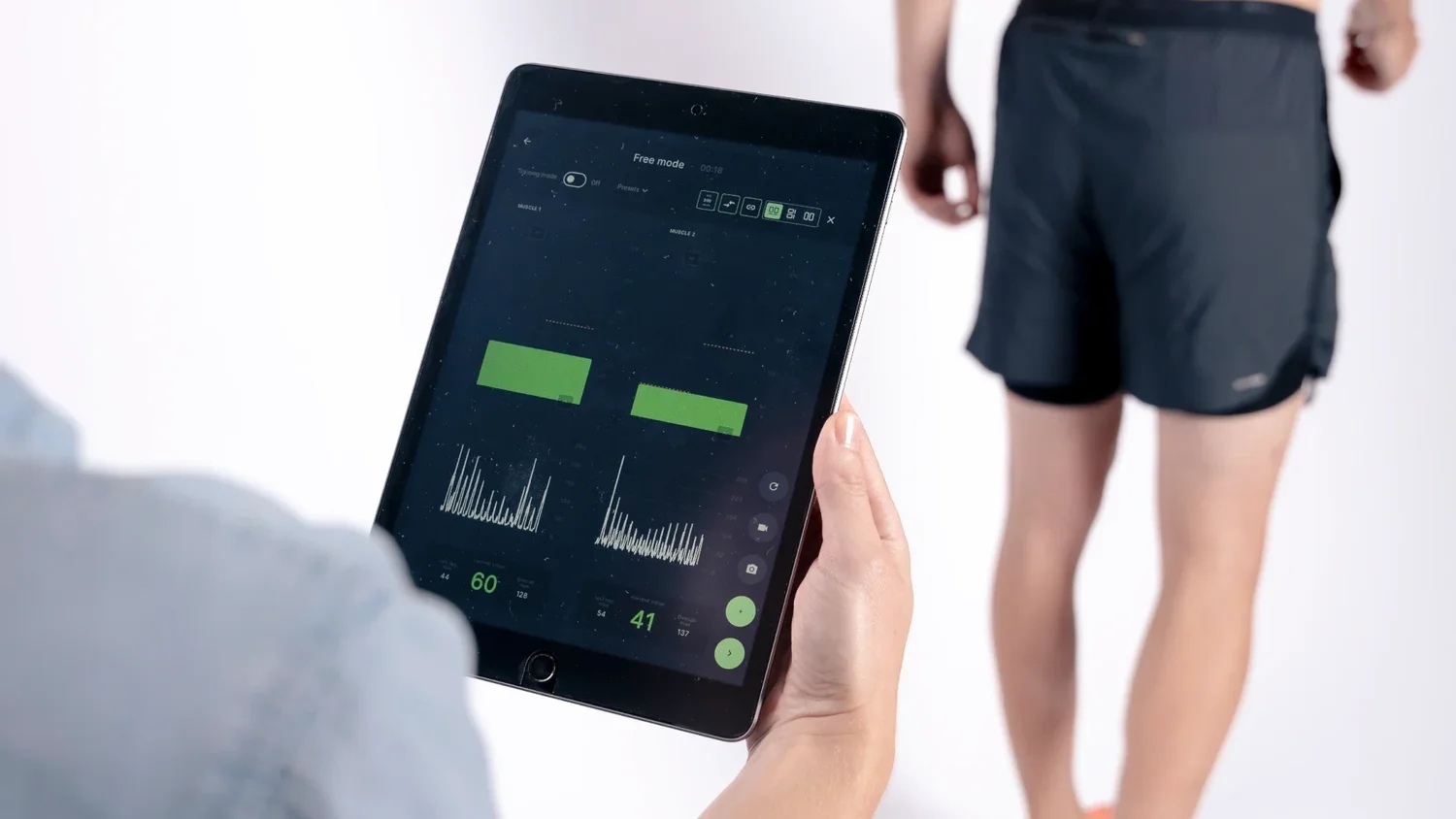 Tablet mit der Anzeige der Muskelaktivität, im Hintergrund die Beine der behandelten Person