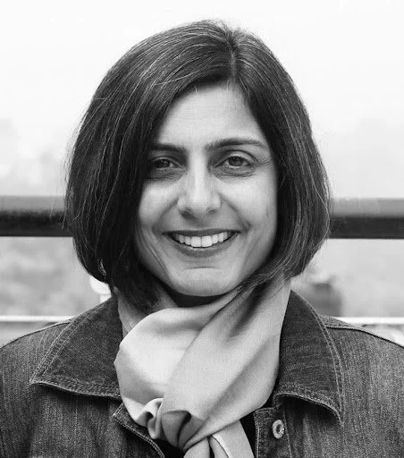 Black and white photo of a woman with shoulder-length hair smiling, wearing a denim jacket and scarf.