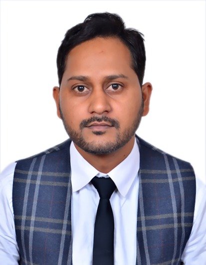 Portrait of a man with short dark hair, a beard, wearing a white shirt, dark tie, and a plaid vest, against a plain white background.