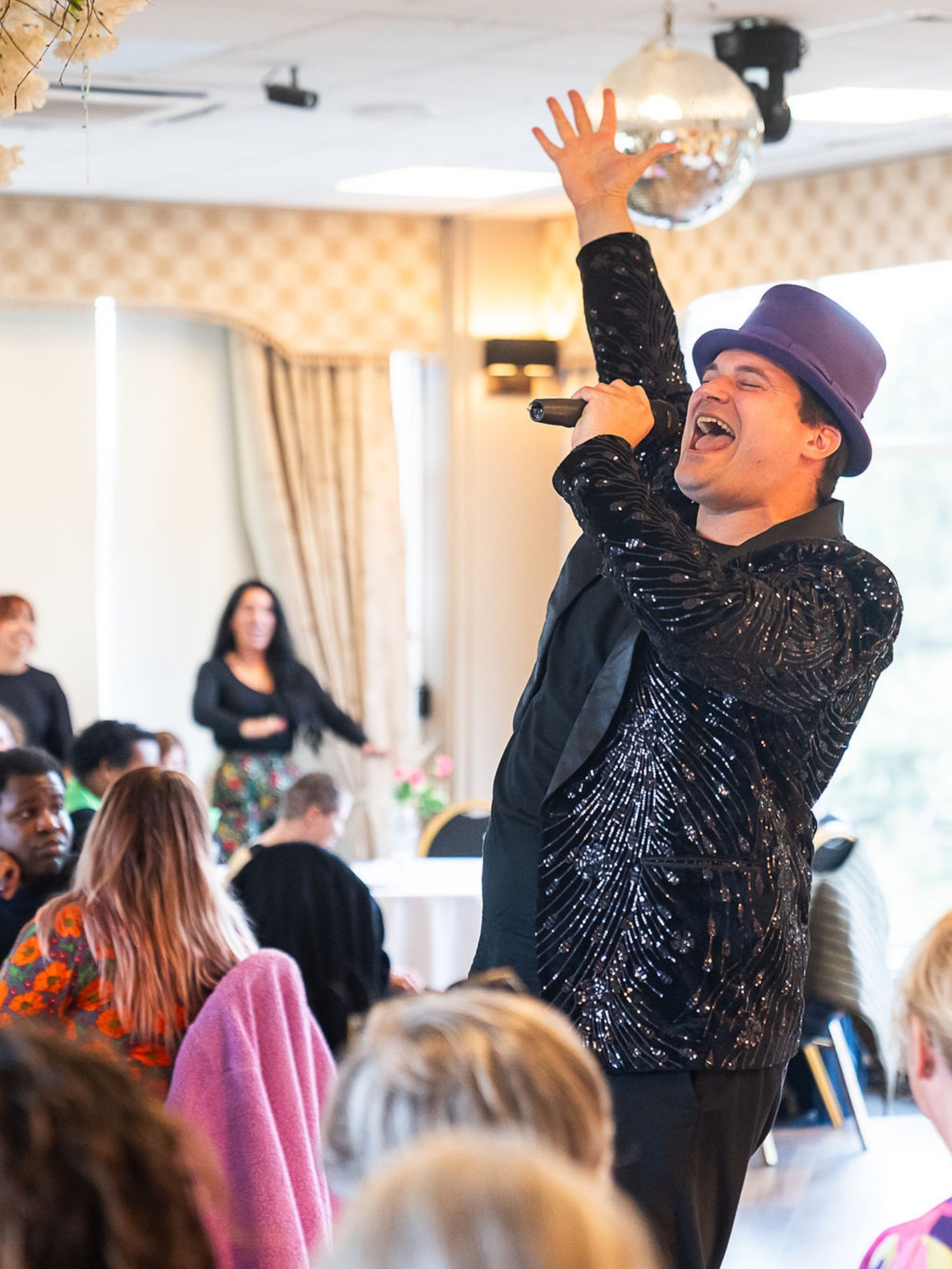 Person in sparkly black jacket and top hat singing to a large crowd.