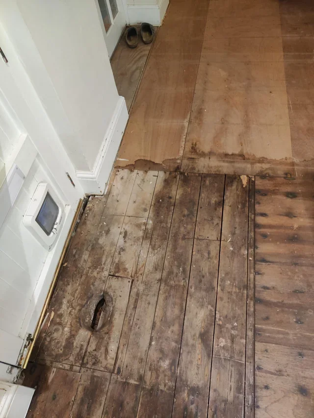 רצפת פרקט ישנה עם לוחות פגומים ורקובים באזור הכניסה לבית