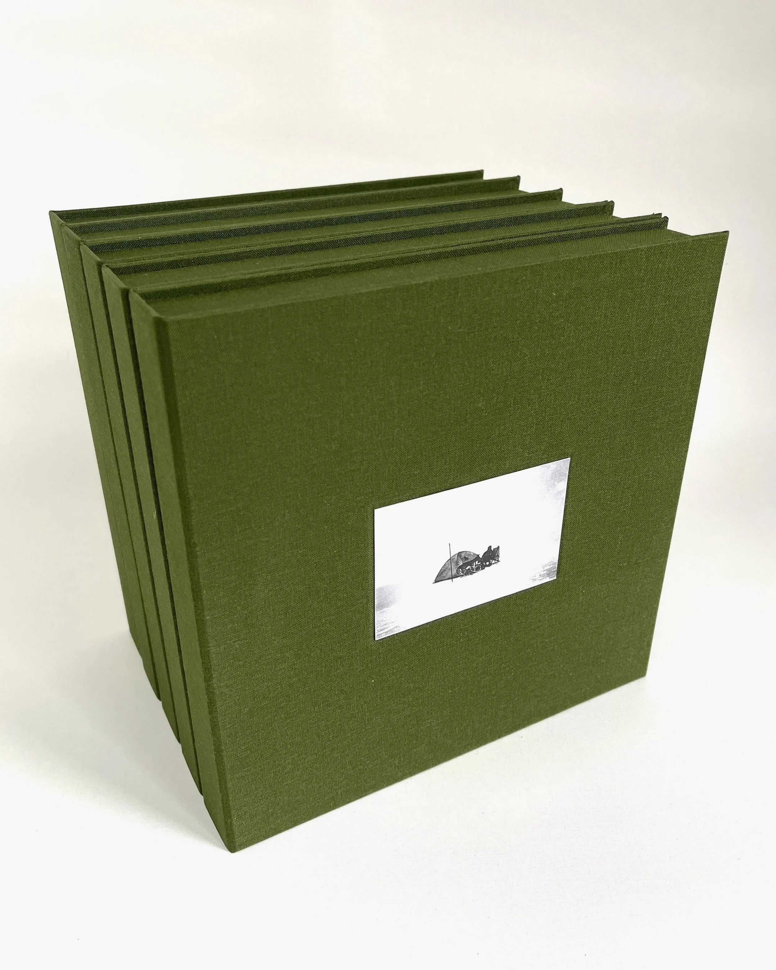 Green photo album with a small black and white photo on the cover showing a boat with an umbrella.