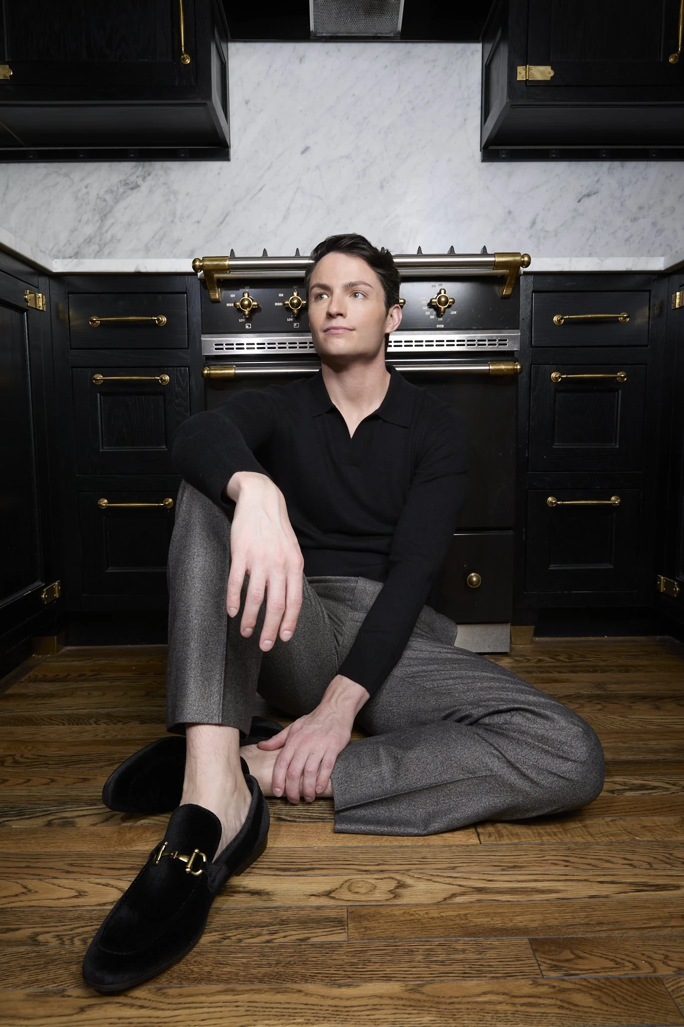 Michael D. Hughes seated on a wooden floor in a dark editorial set