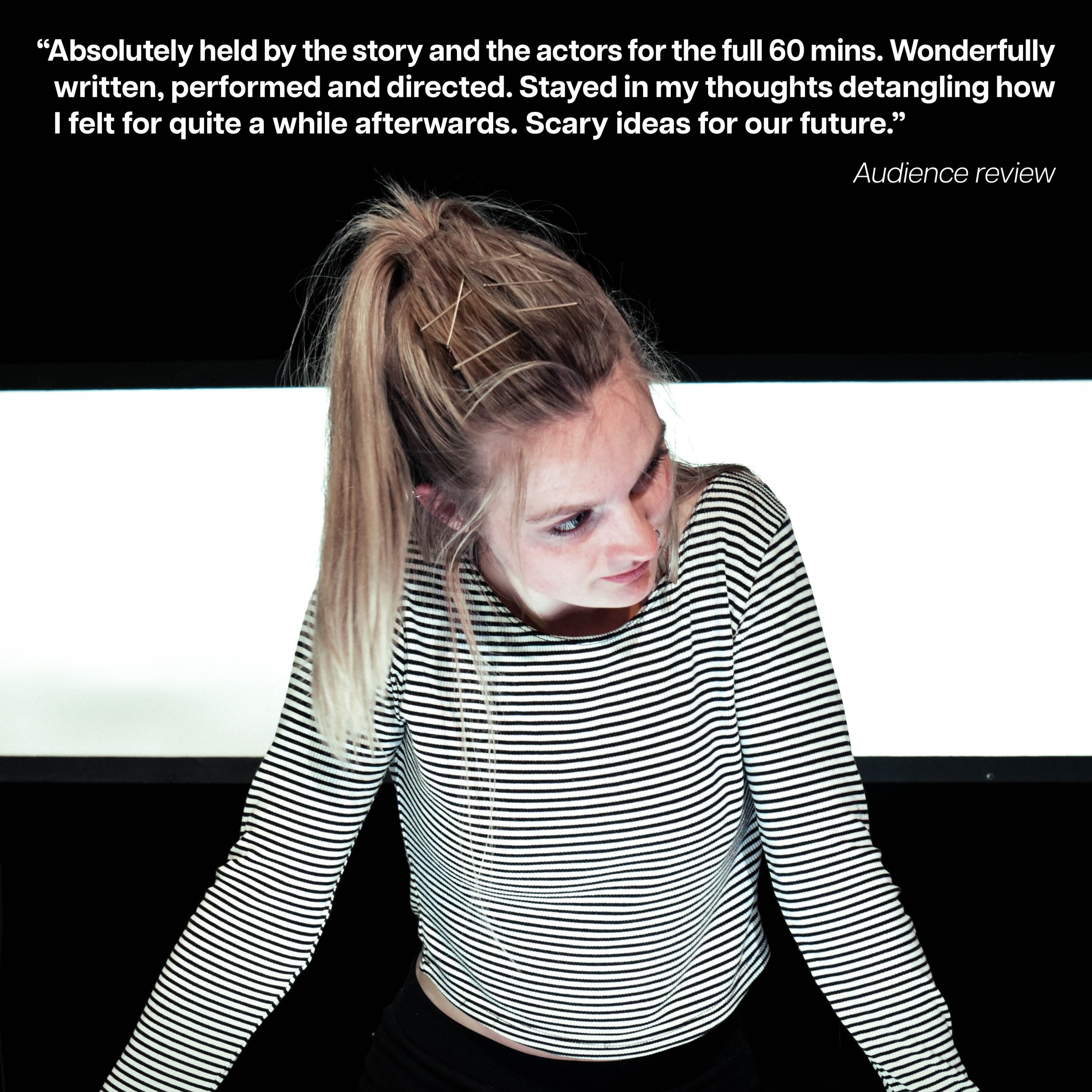 A young woman with blonde hair, styled in a high ponytail secured with hairpins, wearing a black and white striped long-sleeve shirt, leaning forward against a surface, looking to her left with a serious expression in front of a black and white backg