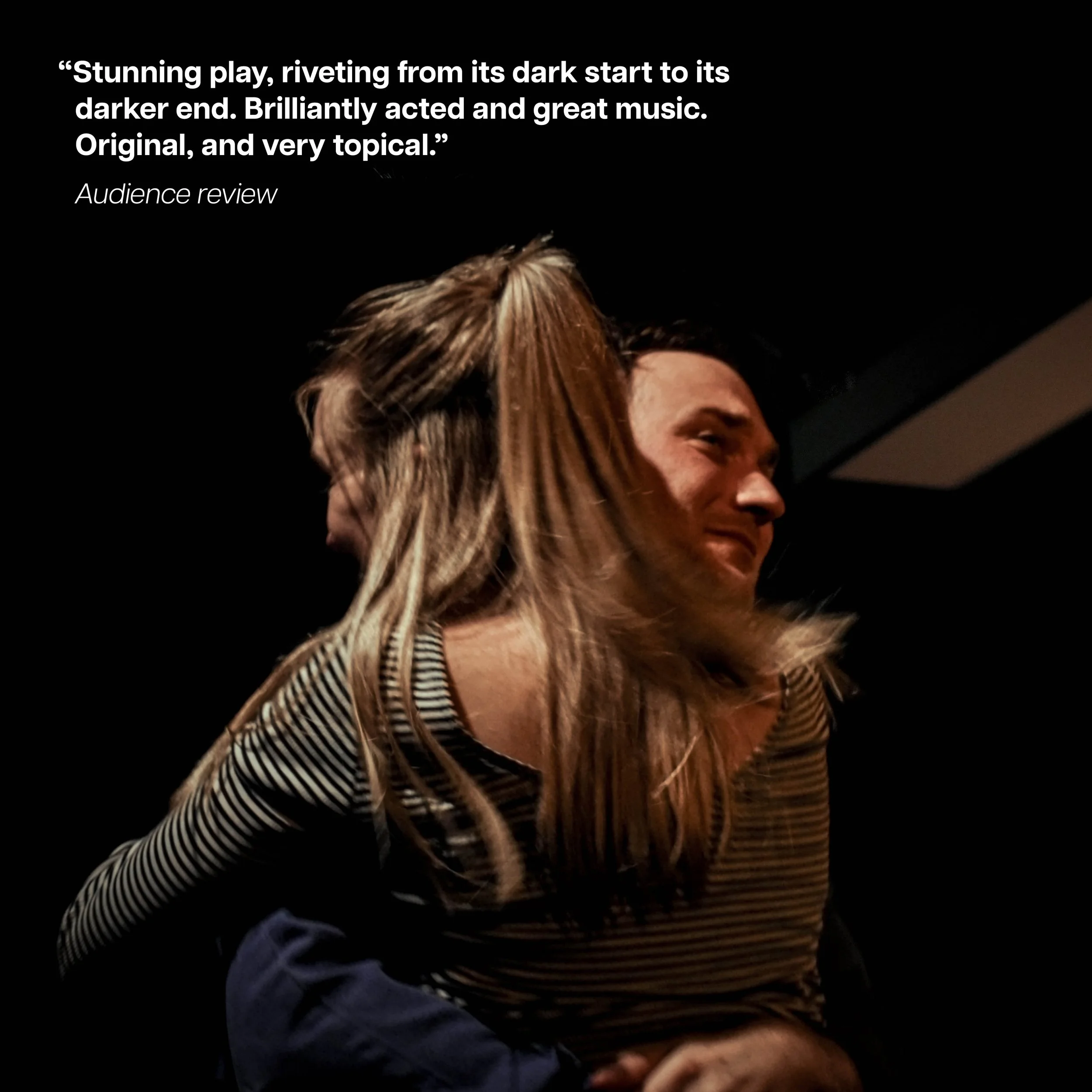 A couple hugging, with the woman having long wavy hair and wearing a striped shirt, and the man having short dark hair and smiling, against a dark background.