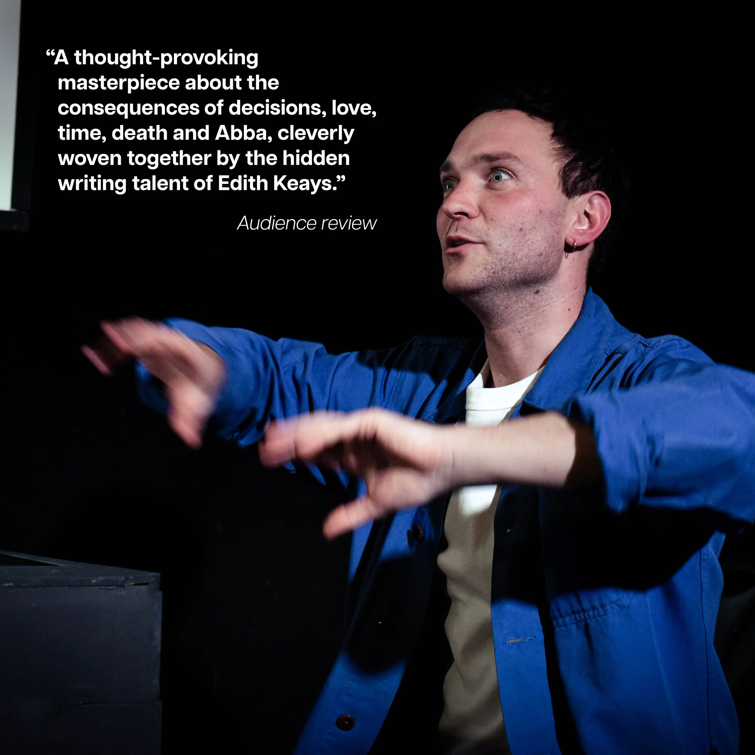 A man with short dark hair, wearing a blue jacket and earrings, gesturing with his hands while speaking or performing, with a quote on the left side about Edith Keays and written in white text on a black background.