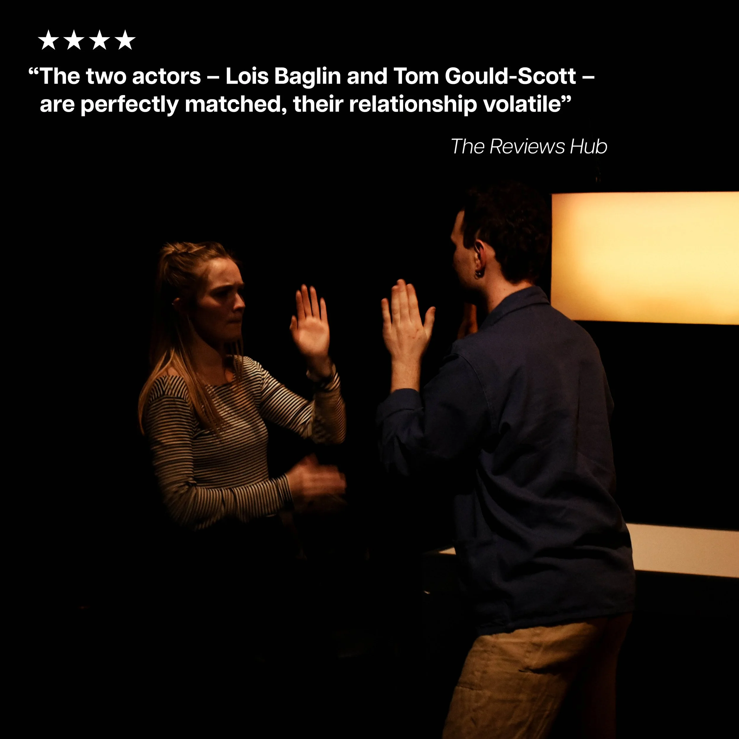 Two actors, a woman with long blonde hair and a man with dark hair, are facing each other with raised hands in a theatrical scene, against a dark background with a white wall lamp and the quote, 'The two actors - Lois Baglin and Tom Gould-Scott - are