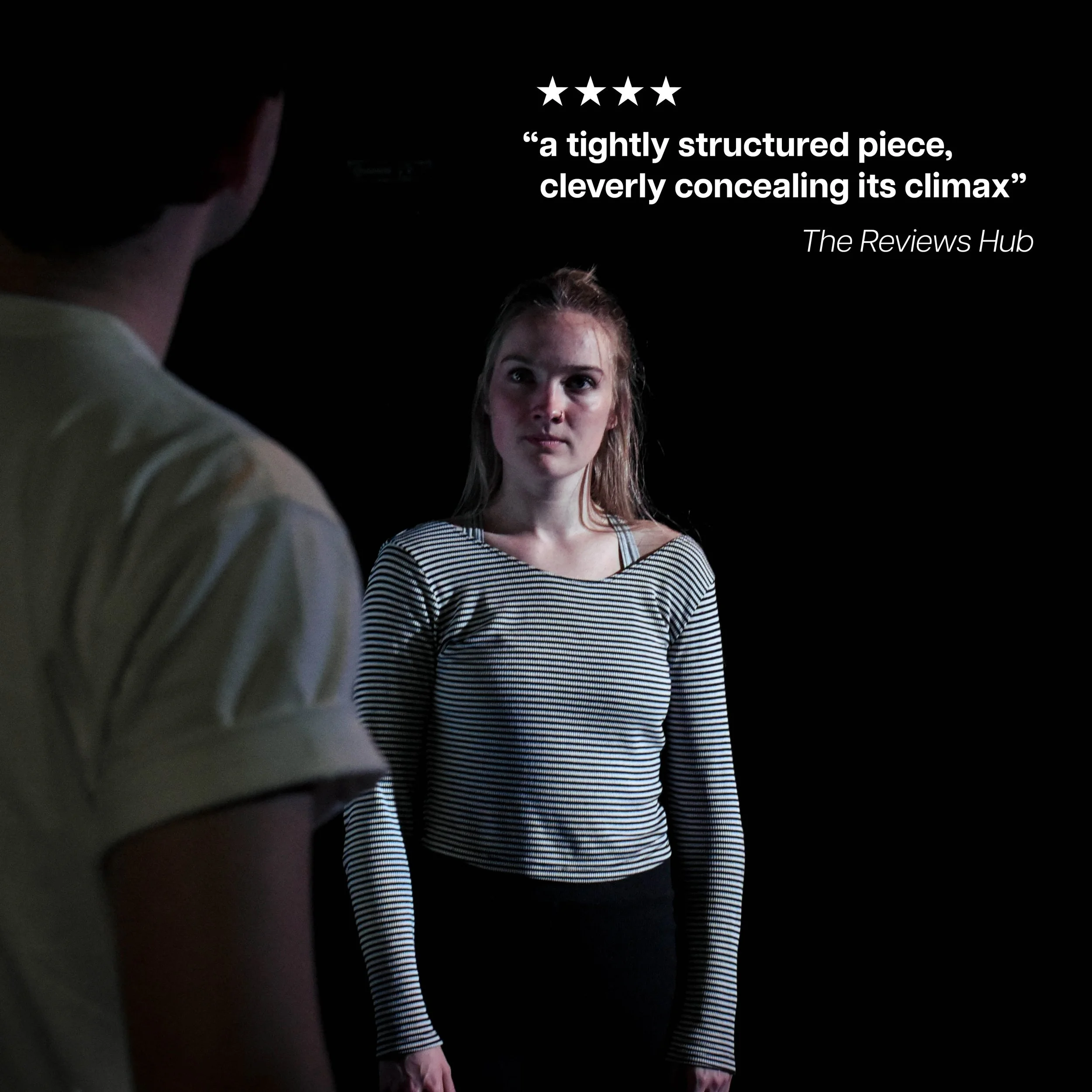 A young woman with long blonde hair wearing a striped long-sleeve shirt stands against a black background, looking at a person partially visible in the foreground wearing a light-colored shirt. There is a quote and review rating in white text in the 