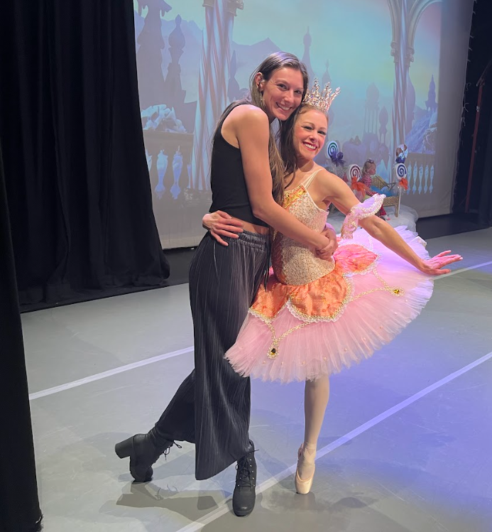Author in pink tutu and huge crown hugs a taller friend dressed in black