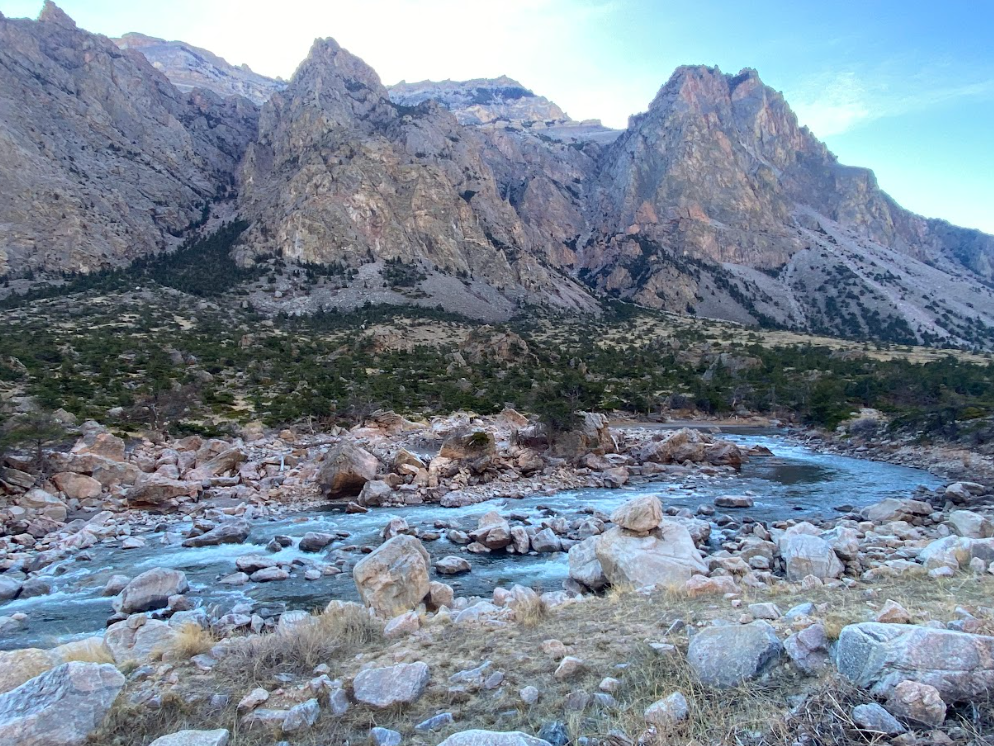 a river runs through a very rocky area with trees and tan jagged cliffs in the background