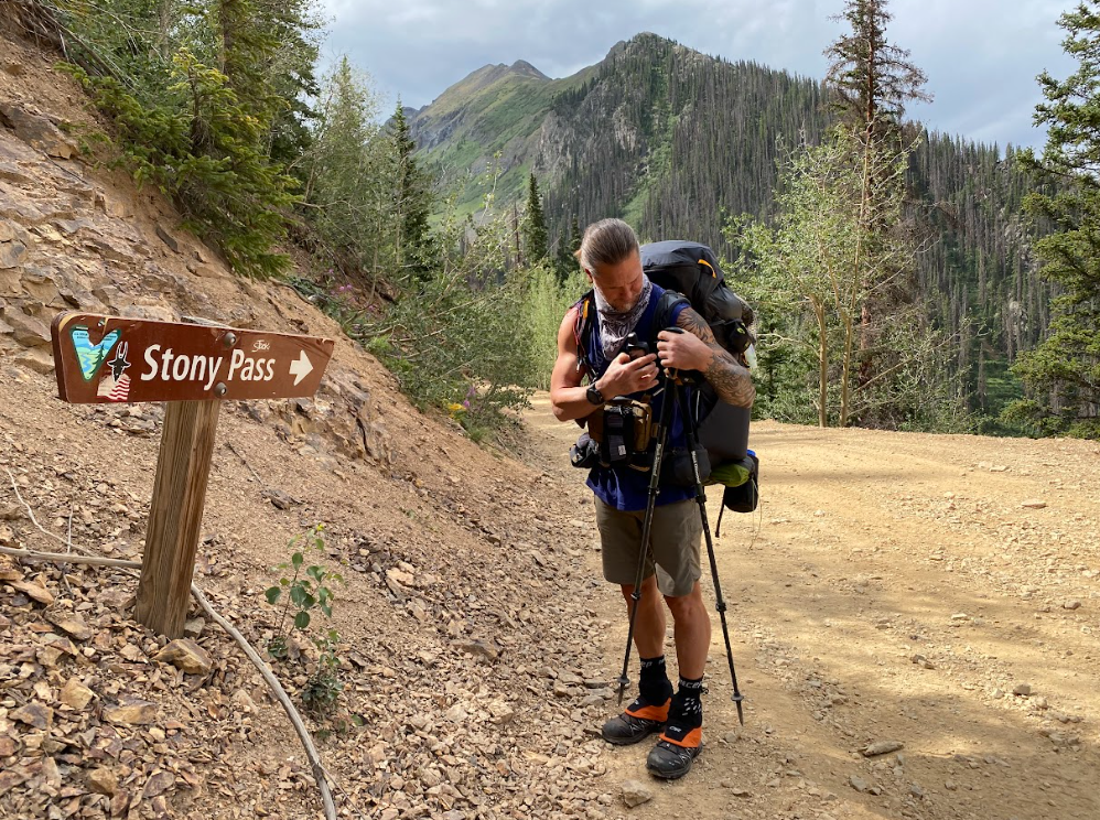 man checks hiking gear next to a sign that states Stony Pass with an arrow