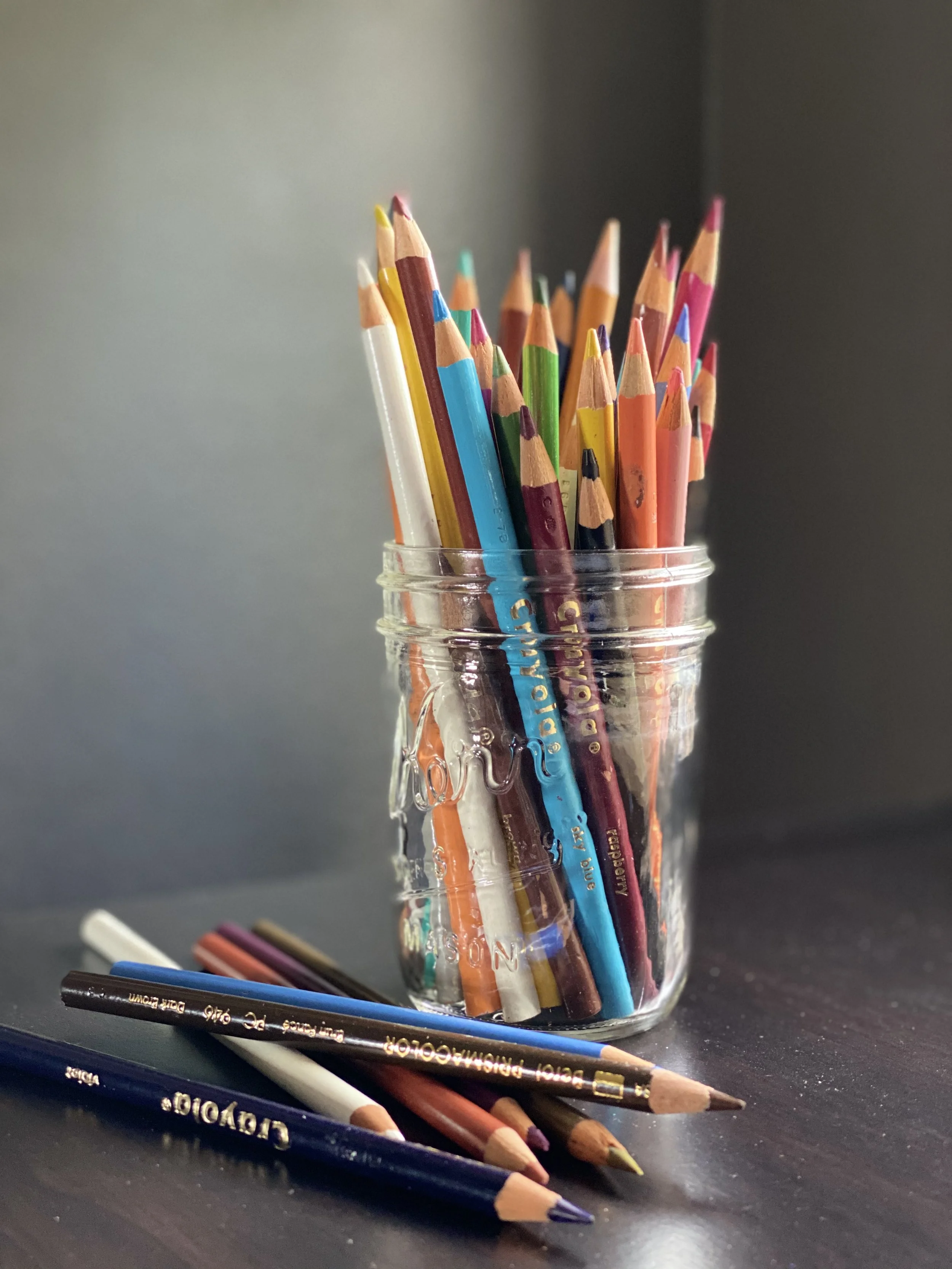 a handful of colored pencils lie next to a jar full of colored pencils