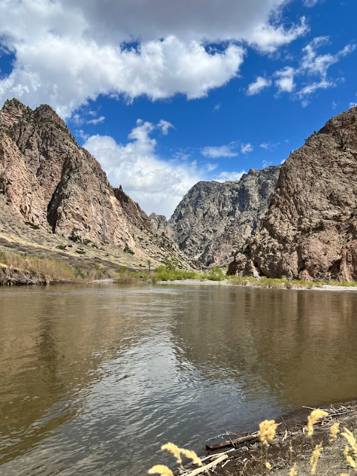 a murky river with reddish brown craggy rocks on the other bank