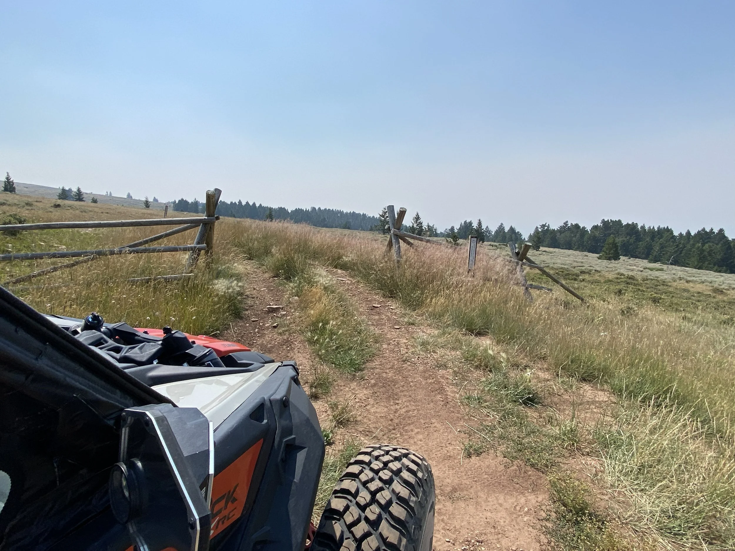 view view from an orange and grey UTV shows off a dirt trail running between ranch style fences which leads across a prairie